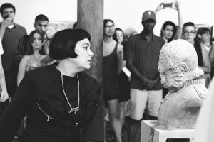Black and white image of woman slapping a white clay bust.