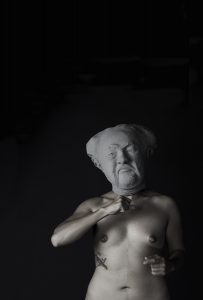White figure with head of a sculpture on black background.
