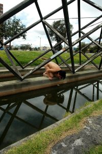 Nude women looking into canal with water and metal geometric structures.