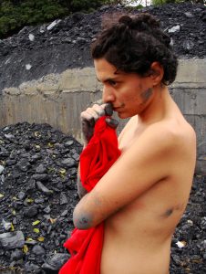 Nude women with red shirt in area of water/pollution drainage.