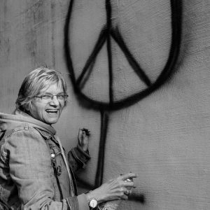 Black and white image of woman spray painting peace sign on wall.