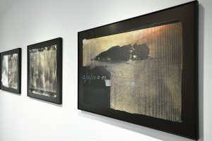 Installation view of three photographs with black frames, figures and seismic register lines.